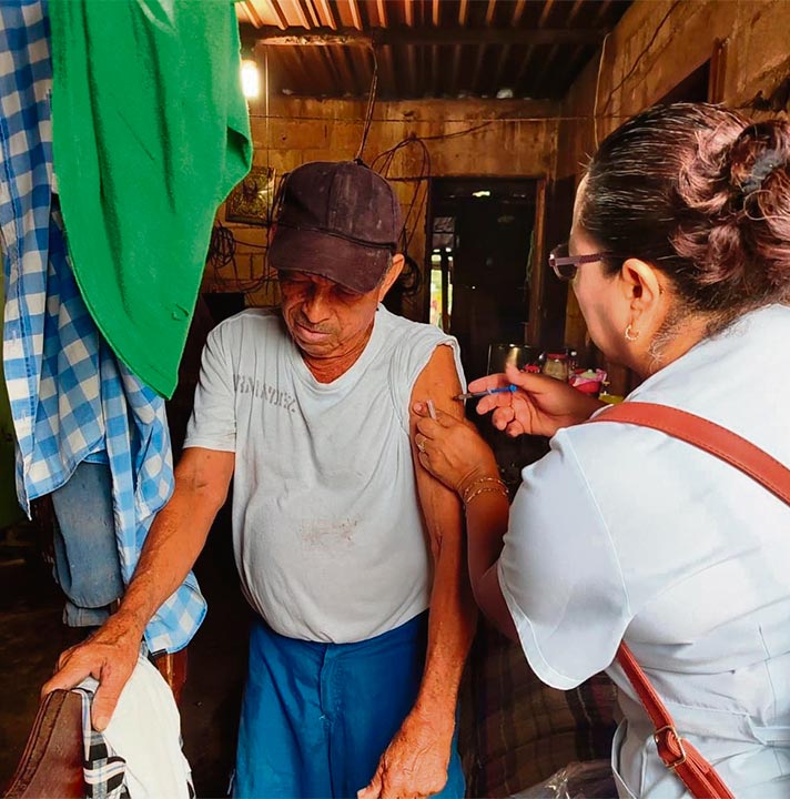 Enfermera vacunando a señor mayor dando servicio en el hogar de la persona vacunada